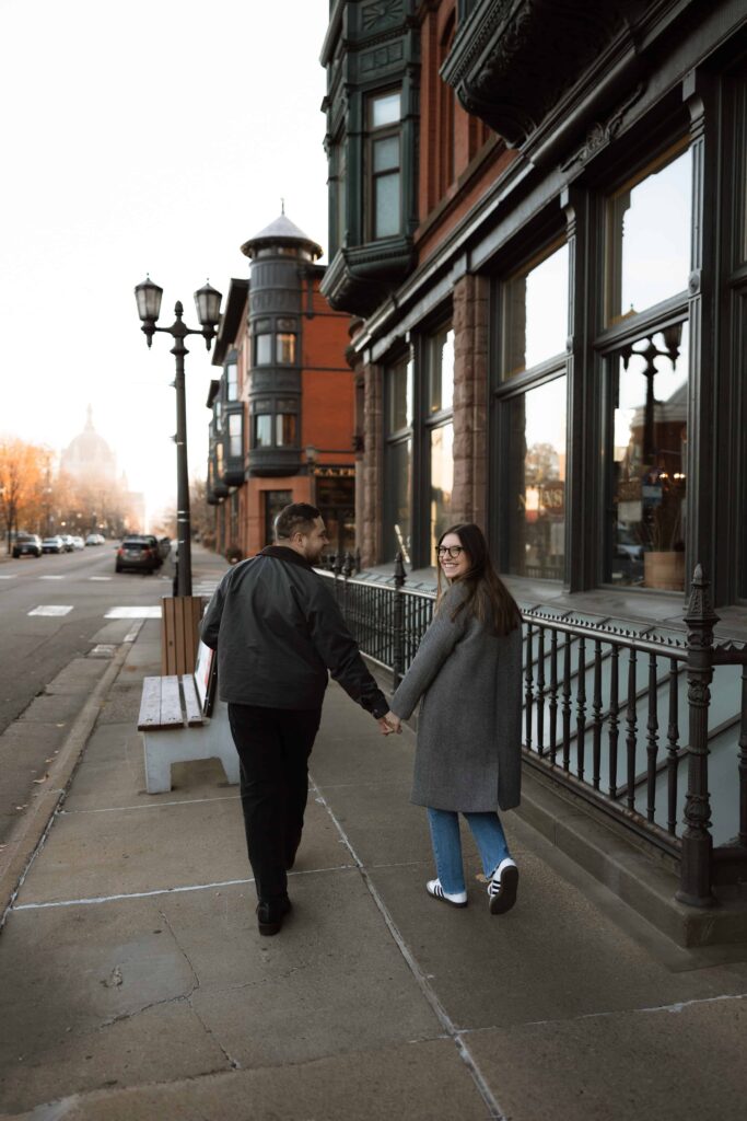 Woman looks back at the camera as she holds her fiance's hand.