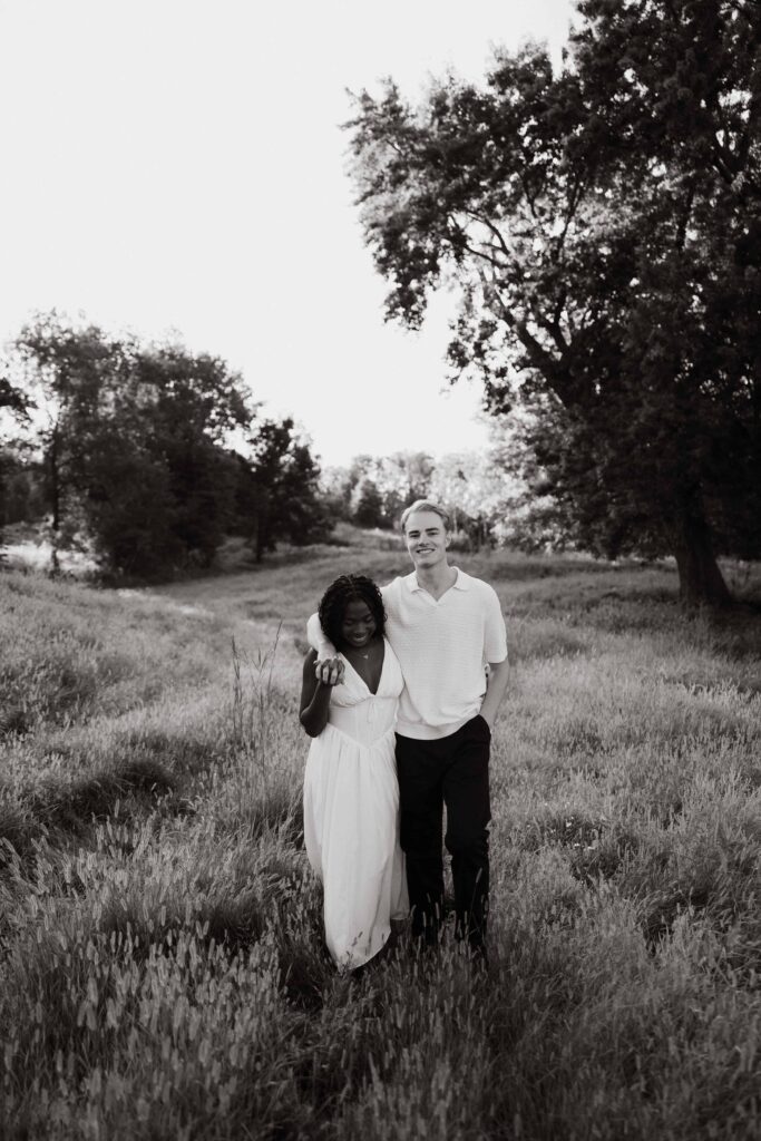 Engaged couple walking in an open field as the glowy sun illuminates them.
