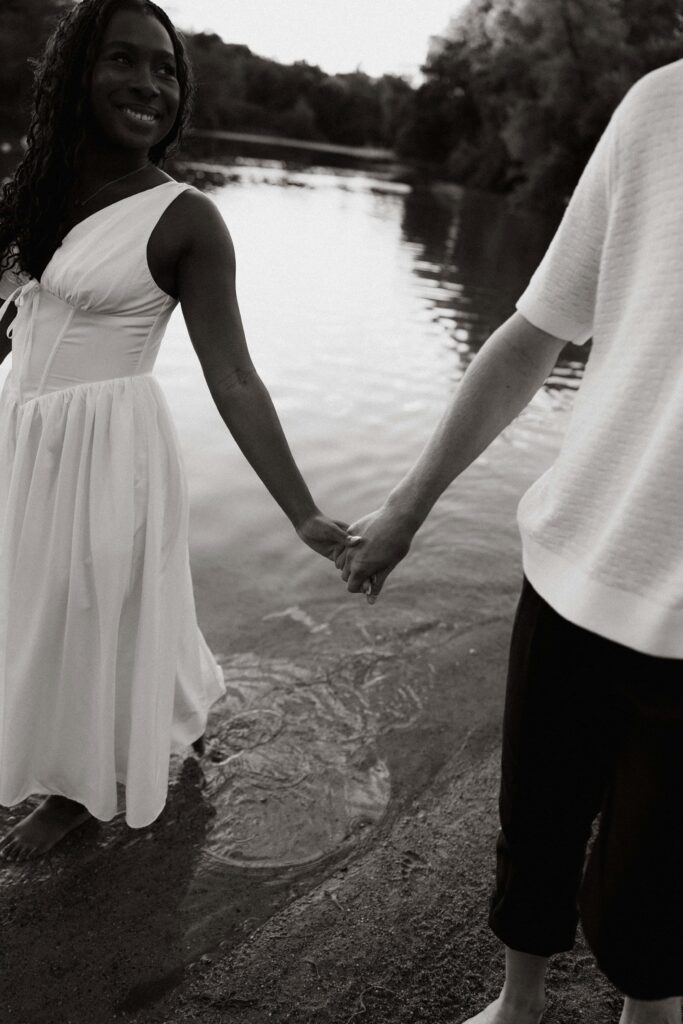 Engaged couple hold hands as they walk through water at a park in Minnesota.