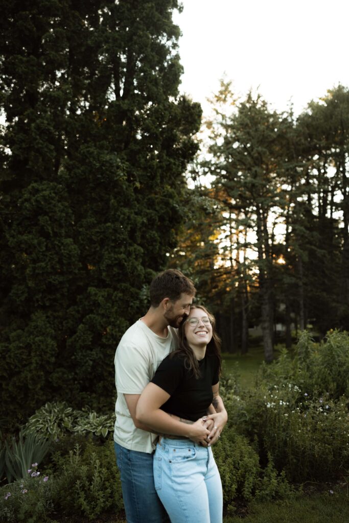 Man hugs his fiance from behind as she smiles.