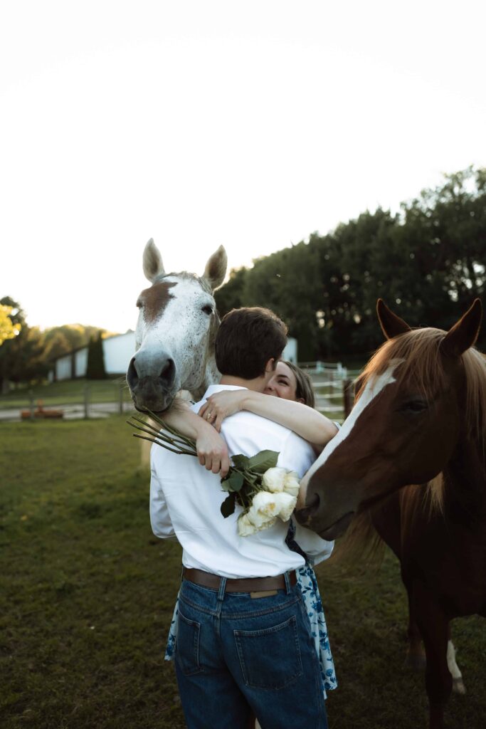 Engaged couple hug as horses surround them during their documentary style engagement session.