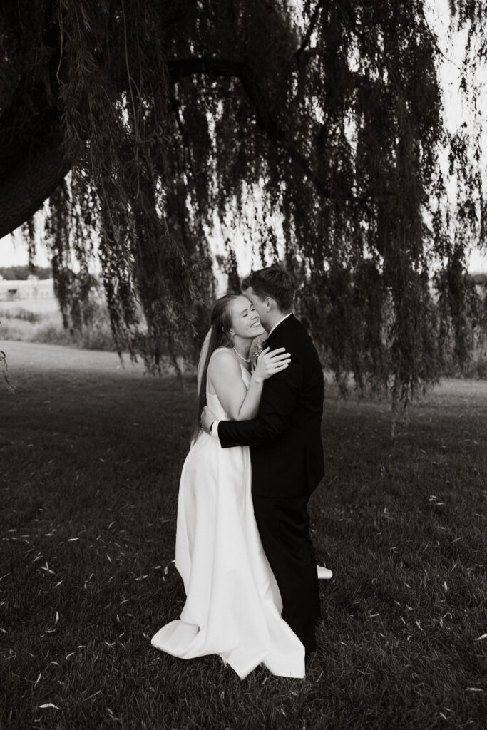 Bride smiles as the groom hugs her and kisses her neck.