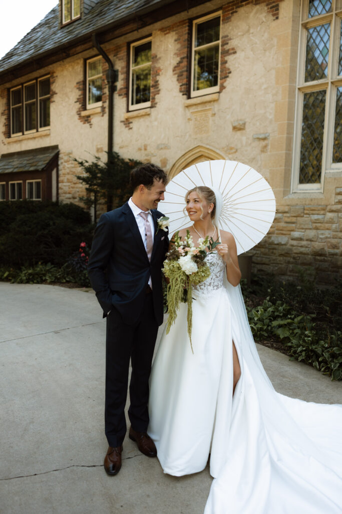 Bride and groom smile at each other during their wedding portraits in front of Plummer House.