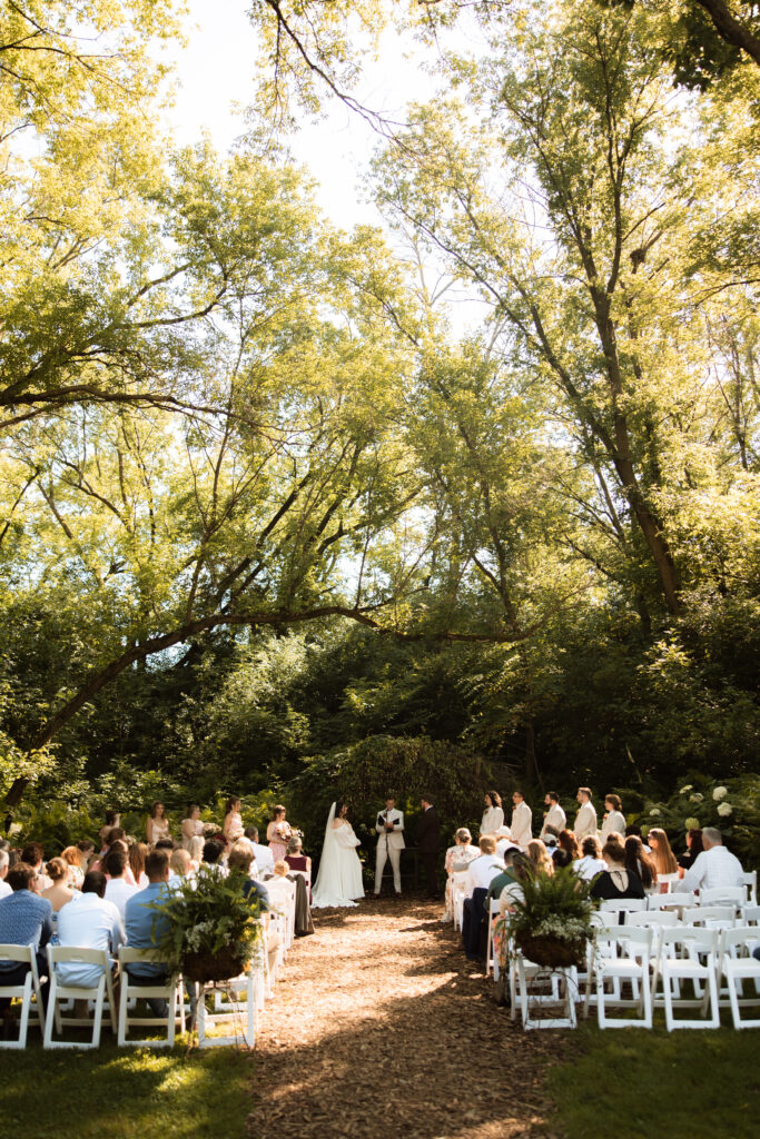The sun streams through the large trees during a wedding ceremony at Camrose Hill Flower Farm.