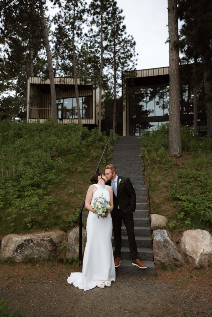 Bride and groom kiss while standing on the stairs at Catalyst in Nisswa, Minnesota.
