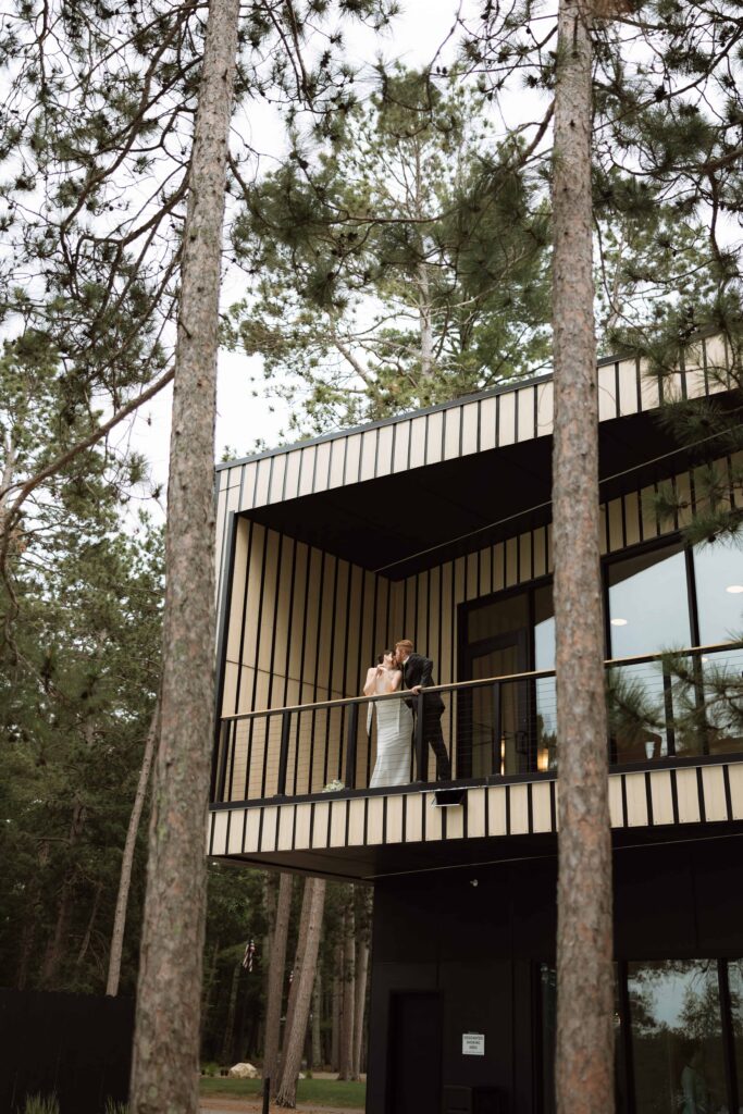 Bride and groom kiss on the balcony of Catalyst by Nature Link in Nisswa, Minnesota.