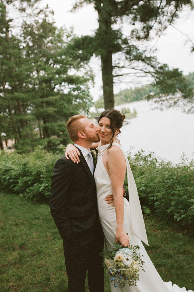 Bride and groom hug while the groom kisses the brides cheek on 35mm film.