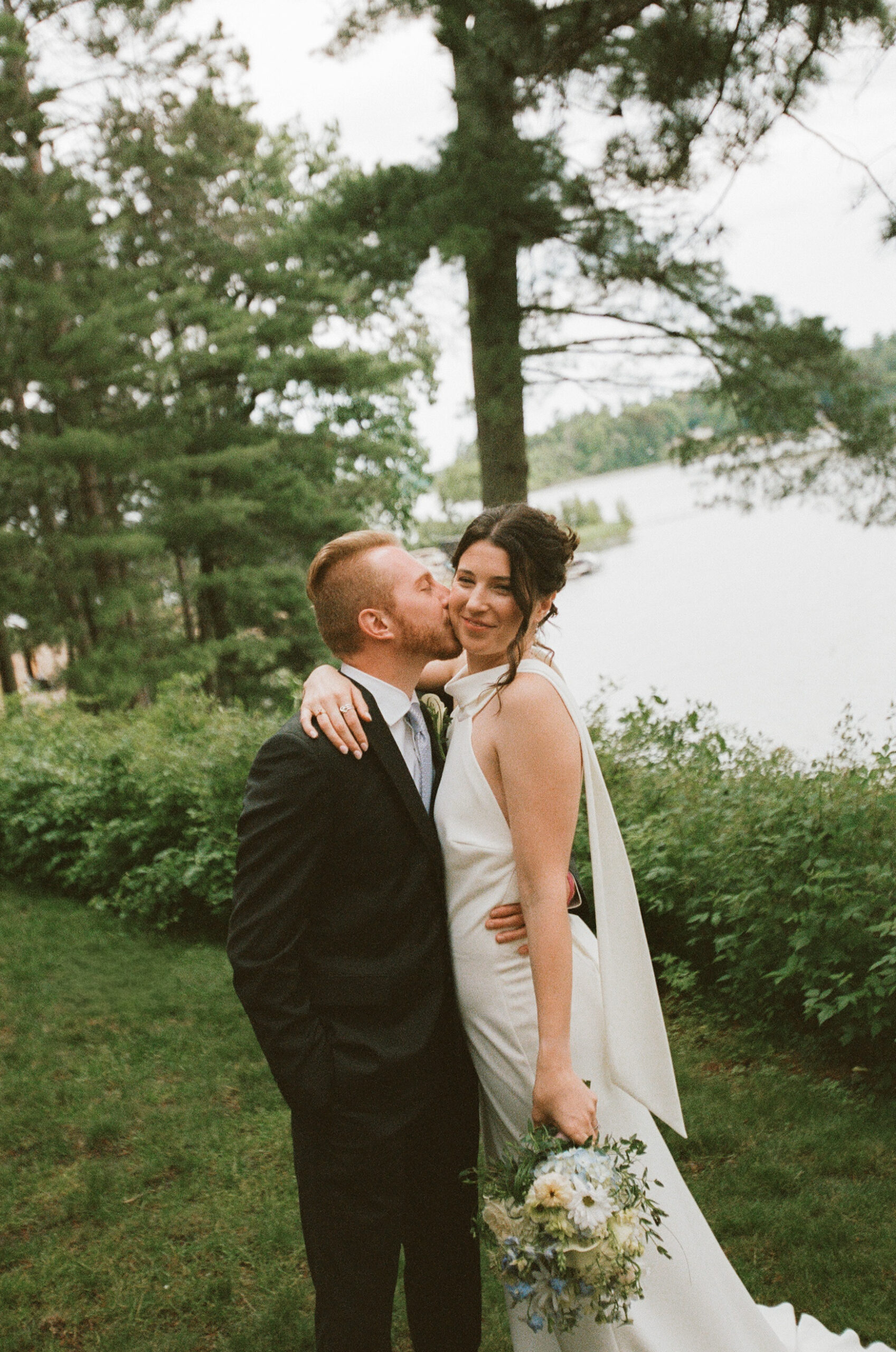 Bride and groom hug while the groom kisses the brides cheek on 35mm film.